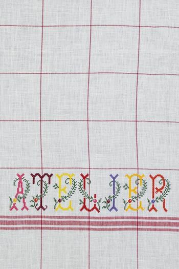Nahansicht des in Rot gestickten Wortes ATELIER auf dem rot karierten Sajou Geschirrtuch aus Ecru Leinen